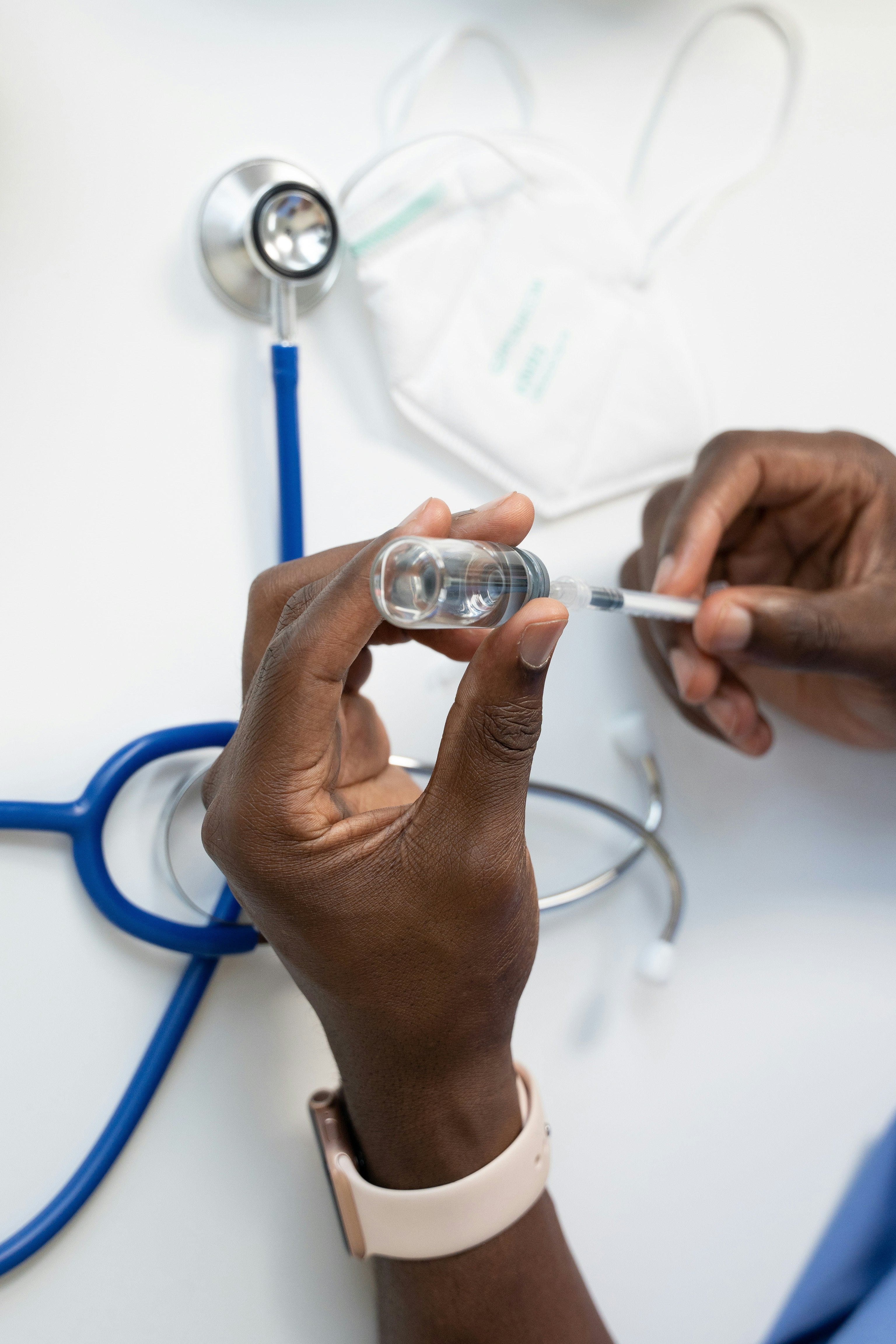 Person holding a syringe with a stethoscope in the background